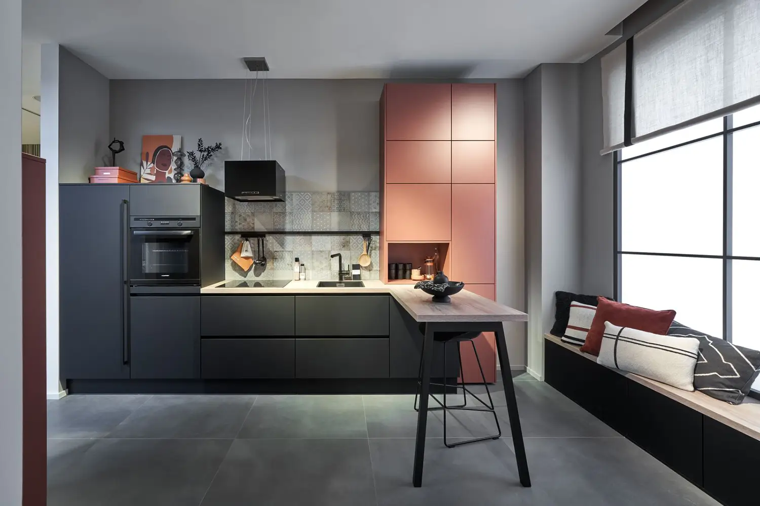 Cuisine noire mate avec colonne rose et bar haut convivial avec tabouret.